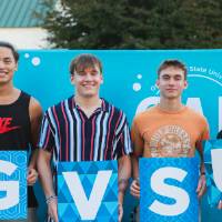 four students posing in front of photo backdrop at Laker Kickoff photo booth and holding GVSU letter signs